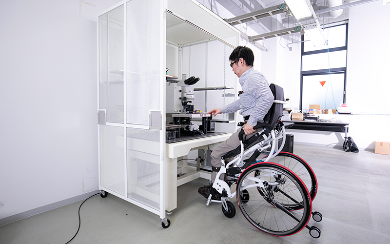 Associate Professor Namiki prepares to peer through a microscope while in his standing-style wheelchair。