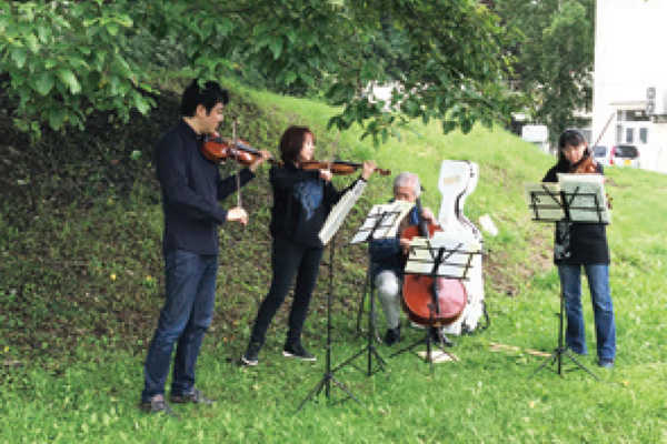 アートラボを担当する近藤薫特任教授ほか2名が森の中でバイオリンを演奏している写真